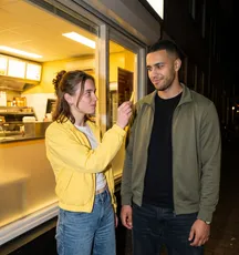 Bij de snackbar houdt iemand een frietje omhoog voor een vriend.